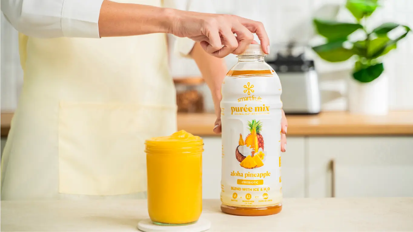 Bottle of Smartfruit Puree Mix being held next to a glass of prepared smoothie