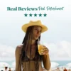 A woman wearing a straw hat stands on a sunny beach while drinking a bright tropical refresher through a straw. Text above reads “Real Reviews, Real Refreshment” with five stars.