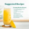 A creamy tropical drink served in a tall glass filled with ice and garnished with mango pieces. Text shows a suggested recipe called Creamy Revive Breeze made with Smartfruit Revive Passion Fruit Mango Star Fruit, water, vanilla plant-based milk, ice, and freeze-dried mango.