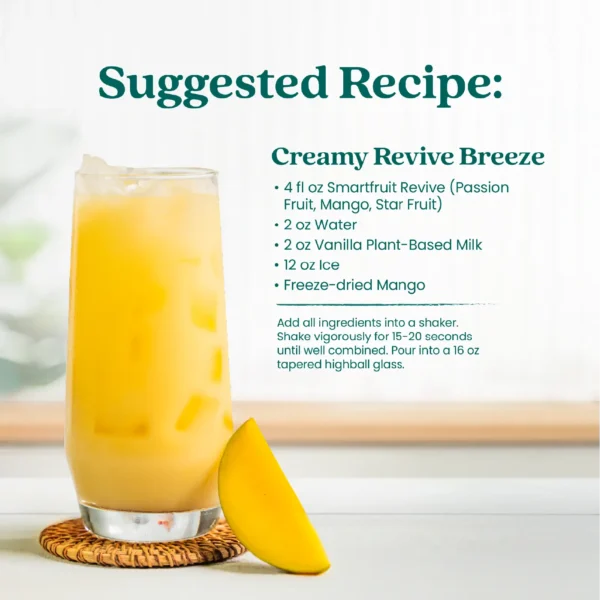 A creamy tropical drink served in a tall glass filled with ice and garnished with mango pieces. Text shows a suggested recipe called Creamy Revive Breeze made with Smartfruit Revive Passion Fruit Mango Star Fruit, water, vanilla plant-based milk, ice, and freeze-dried mango.