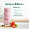 A creamy pink strawberry drink served in a tall glass with ice and fresh strawberries beside the glass. Text shows a suggested recipe called Pink Drink made with Smartfruit Renew Refresher, vanilla plant-based milk, water, crushed ice, and freeze-dried strawberry.