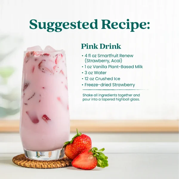 A creamy pink strawberry drink served in a tall glass with ice and fresh strawberries beside the glass. Text shows a suggested recipe called Pink Drink made with Smartfruit Renew Refresher, vanilla plant-based milk, water, crushed ice, and freeze-dried strawberry.