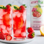 2 glasses of Lemon Blush on a serving plate surrounded by strawberries, a lemon, and a bottle of Smartfruit