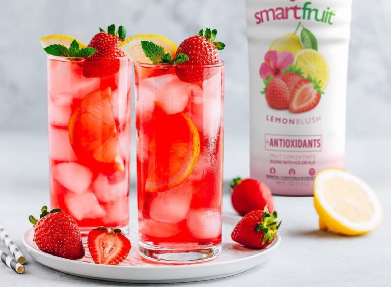 2 glasses of Lemon Blush on a serving plate surrounded by strawberries, a lemon, and a bottle of Smartfruit