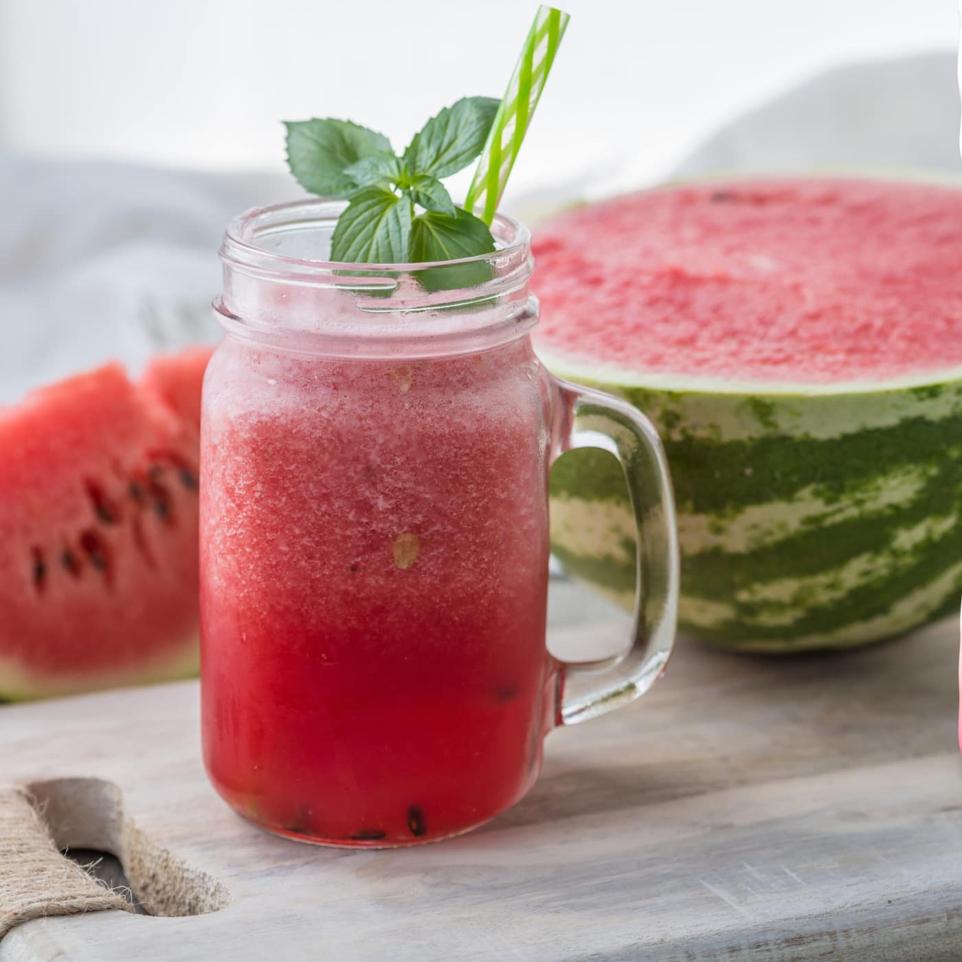 A refreshing watermelon drink garnished with mint in a mason jar, with a halved watermelon and slices in the background.