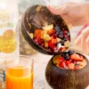 Coconut bowls containing fruit next to a glass of juice