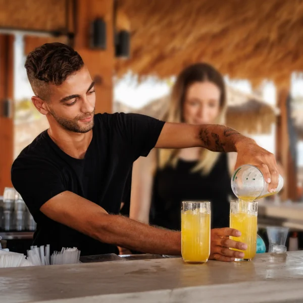 Man pouring drinks from a shaker into two glasses with a woman looking on
