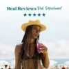 A woman wearing a straw hat at the beach drinks a pink refresher beverage through a straw. Text above reads “Real Reviews, Real Refreshment” with five stars.